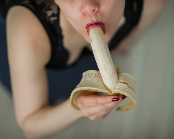 Блондинка в чорній мереживній білизні еротично їсть банан. Приваблива жінка з чуттєвими червоними губами сексуально смокче і випускає банан. Усна насолода. крупним планом . — стокове фото