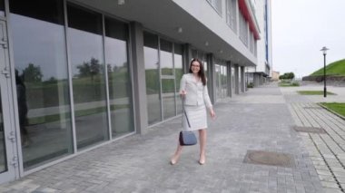 Ceketli ve etekli bir kadın açık havada mutlulukla oynaşıyor. Gözlüklü ve takım elbiseli bir kız sokakta yürüyor ve dans ediyor..