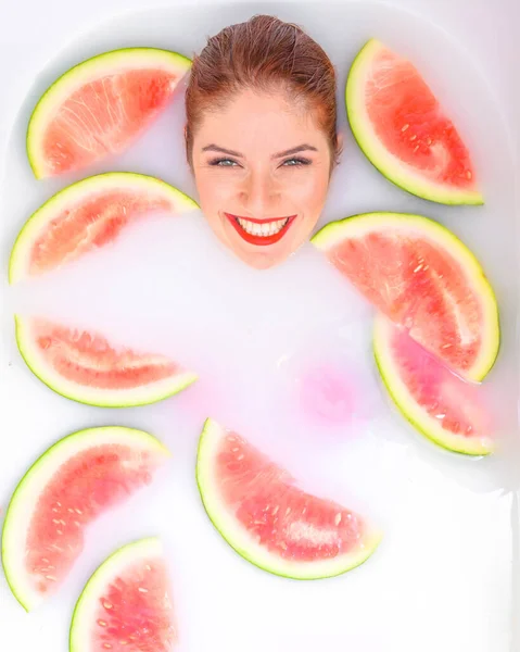 Portret van een mooie roodharige vrouw neemt een bad met melk en plakjes watermeloen. Spa behandeling voor huidverjonging en voeding. Rijpe plakjes van de grootste bes. — Stockfoto