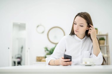 Beyaz gömlekli genç esmer, bir kafede iş ortağı bekliyor. İş toplantısındaki bir kadın. Kız molada kahve içiyor ve SMS okuyarak akıllı telefon kullanıyor..