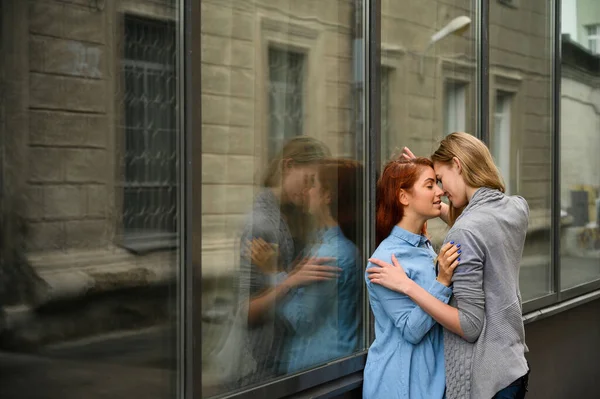 Relaties van hetzelfde geslacht. Portret van twee jonge lesbiennes die hartstochtelijk knuffelen en tegen een spiegelwand staan. Houden van paar gay vrouwen staan op de straat en tonen gevoelens. — Stockfoto