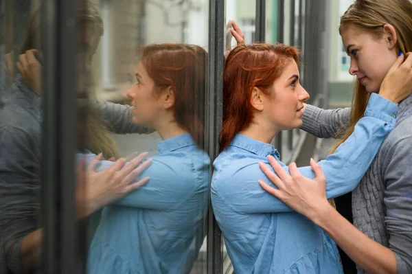 Samkönade förhållanden. Porträtt av två unga lesbiska står på gatan och kysser varandra. En ung kvinna trycker passionerat sin älskare mot en spegelvägg. — Stockfoto