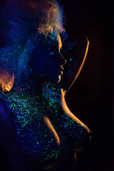 Trucco del diavolo. Bella donna di profilo nella body art ultravioletta, brilla al buio. Ragazza è dipinta in polvere fluorescente . — Foto Stock
