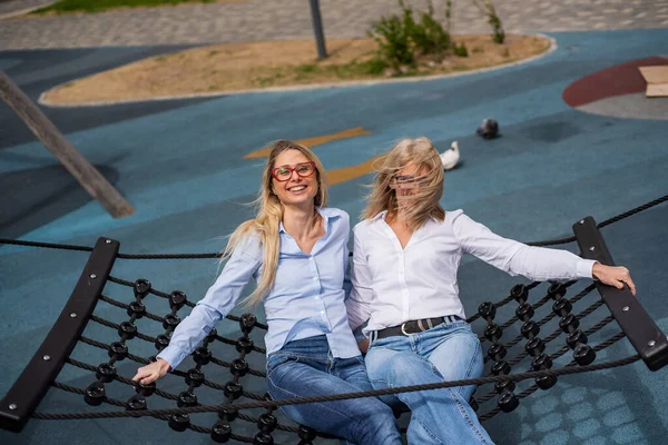 Žena středního věku a její starší matka se houpají v houpací síti. Špatné vidění je dědičné. Větrný den. Babička a matka. — Stock fotografie