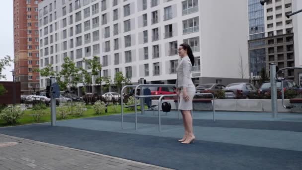 A woman in a business suit and heels does a sit-up outside. Business woman in glasses doing exercises on the buttocks during a lunch break. — Stock Video