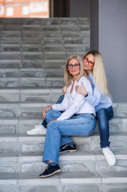 Gözlüklü güzel bir sarışın ve olgun annesi dışarıda merdivenlerde oturuyor. İyi giyimli yaşlı bir kadın yetişkin kızına sıkıca sarılır. Aşk ve aile değerleri. Anneler Günü.