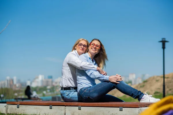 Twee verrassend gelijkaardige vrouwen zitten op een bank in een omhelzing en glimlachen. Een vrouw van middelbare leeftijd en haar oudere moeder. Mooie goed verzorgde moeder en dochter familie look. — Stockfoto