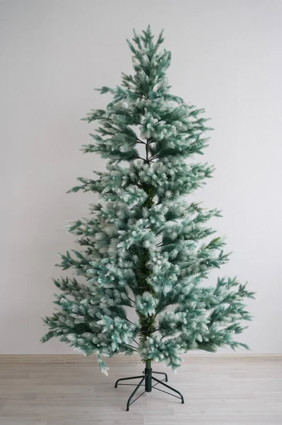 Arbre artificiel écologique pour la nouvelle année. Un arbre de Noël nu sans décorations est debout contre un mur blanc. Traditions pour des vacances en famille habiller une épicéa . — Photo