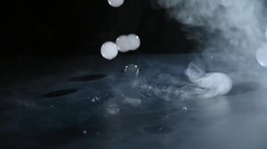 İçinde duman olan sabun köpükleri siyah bir masaya düşer ve patlar. Yavaş Hareket Koyu Arkaplan.