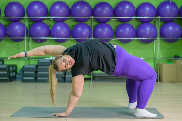 Fat woman is engaged in pilates in a fitness gym. A girl with a lot of overweight trying to lose weight with the help of sports and yoga, does the bridge exercise.