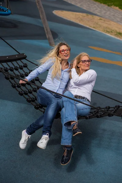 Una donna di mezza età e la sua anziana madre dondolano su un'amaca. La scarsa vista è ereditaria. Giornata ventosa. Nonna e madre . — Foto Stock