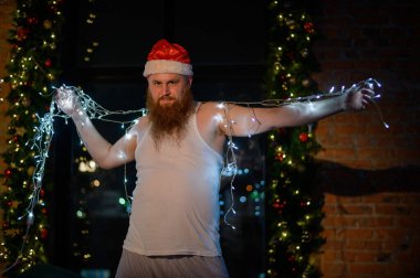 Noel arifesinde Noel Baba 'nın iç çamaşırlı komik bir görüntüsü. Noel Baba kostümü giymiş bir adam yılbaşında ışıklı bir çelenk tutuyor. Bir kadın fotoğraf çekiminin parodisi..