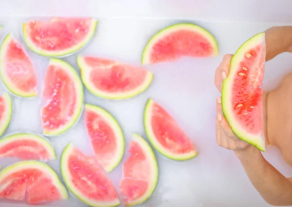 Closeup of womans hands holding a slice of watermelon. Girl takes a bath with milk and fruit to rejuvenate her skin. Body care. — Stock Photo, Image