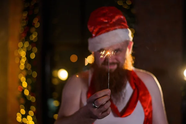 Weihnachtsmann mit Weihnachtsfunkeln im Urlaub. Ein Mann mit rotem Bart und Weihnachtsmannmütze feiert das neue Jahr. Frohes neues Jahr und Weihnachten. — Stockfoto