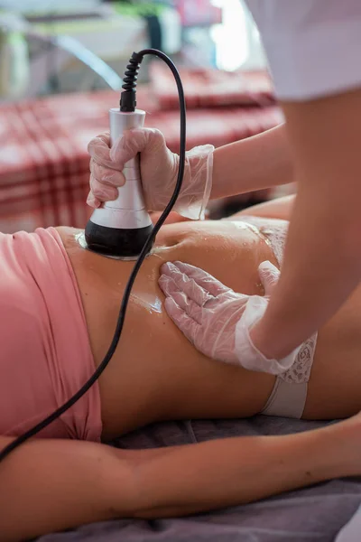 Una mujer se acuesta en un sofá y recibe un masaje de hardware del abdomen. El procedimiento para bajar de peso. Masaje corporal eléctrico . —  Fotos de Stock