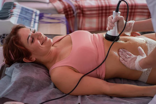Una donna si trova su un divano e riceve un massaggio hardware dell'addome. La procedura per la perdita di peso. Massaggio corpo elettrico . — Foto Stock