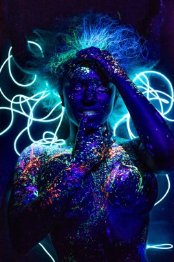 Kız şeytanın görüntüsü, kontak lensler ve boynuzlar. Ultraviyole boyalı kadın. Floresan tozu. Ultraviyole ışıkta parlayan vücut sanatı. Gözlerde yıldızlar..