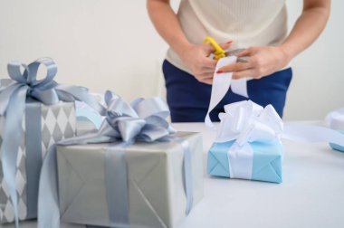 Kadın yeni yıl için hediyelerle kutuları sarar. Kadın eli, yakın plan. Anneler Günü için bir sürpriz hazırlıyor. Doğum için paket kağıdı ve kurdele. Tasarımcı fiyonk bağlıyor..