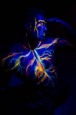 Uv desenleri bir erkek vücut üzerinde dolaşım sisteminin vücut sanatı. Kaslı bir atletin göğsünde, damarlar ve arterler floresan boyalar ile çizilir. Vücut geliştirmeci aynada duruyor.