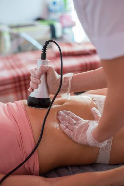 Bir kadın kanepeye uzanır ve karın bölgesine donanım masajı yaptırır. Kilo verme prosedürü. Elektrik vücut masajı..