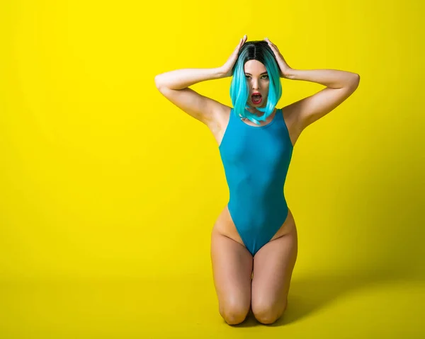 파란 가발을 쓴 아름다운 소녀와 노란 배경에 밝은 비키니를 입은 소녀. 인공털에 수영복을 입은 여자가 엉덩이를 강조하는 모습. — 스톡 사진