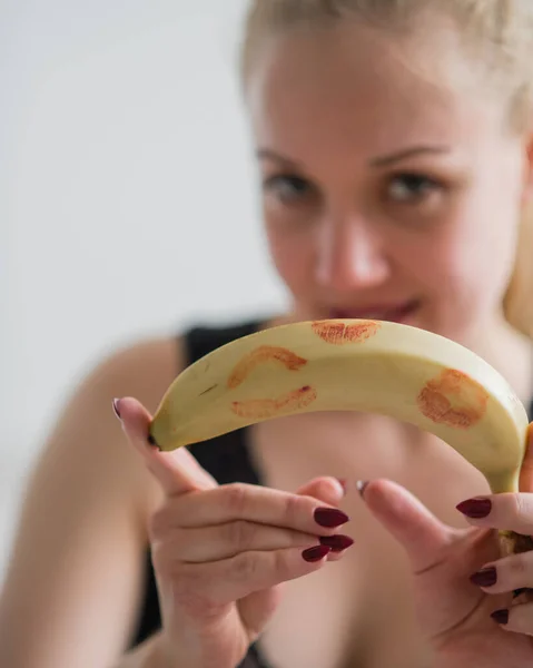Bionda tiene una banana non pelata con segni di rossetto rosso. Il concetto di sesso orale. Uno sguardo seducente. Frutta appetitosa . — Foto Stock