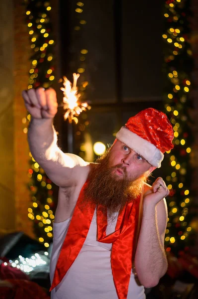 Père Noël avec des étincelles de Noël. Un homme avec une barbe rouge dans un chapeau du Père Noël et un T-shirt pour un alcoolique brûle des étincelles. Parodie. — Photo