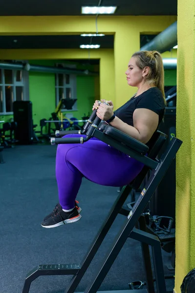 Жирна жінка робить вправи на м'язах черевної порожнини для схуднення. Товста блондинка займається симулятором в спортзалі . — стокове фото