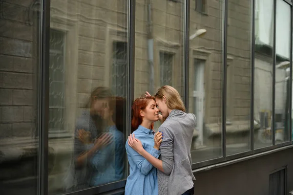Relações entre pessoas do mesmo sexo. Retrato de duas jovens lésbicas apaixonadamente abraçando e de pé contra uma parede de espelho. Amar casal de mulheres gays de pé na rua e mostrando sentimentos . — Fotografia de Stock