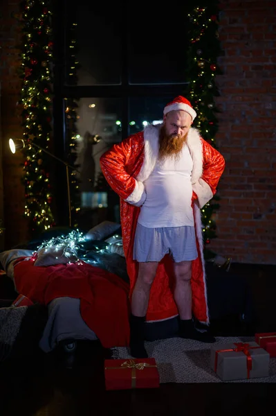 Papá Noel malo solo en Navidad. El hombre agresivo en el traje de Papá Noel en el fondo de las decoraciones de Año Nuevo . —  Fotos de Stock