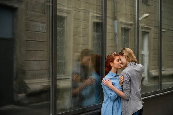 Samkönade förhållanden. Porträtt av två unga lesbiska står på gatan och kysser varandra. En ung kvinna trycker passionerat sin älskare mot en spegelvägg. — Stockfoto