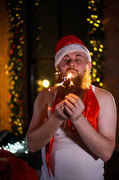 Kerstman met kerst schittert op vakantie. Een man met een rode baard in een kerstmuts viert het nieuwe jaar. Geluk met Kerstmis. — Stockfoto