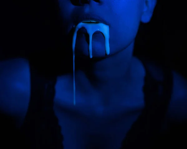 Un espeso líquido blanco fluye por los labios de una joven europea. Goteando. Ultravioleta, luz azul. Retrato de cerca. Escupe. . — Foto de Stock