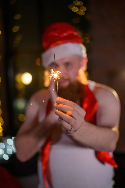 Santa with Christmas sparkles on holiday. A man with a red beard in a Santa Claus hat is celebrating the New Year. Happiness at Christmas. — Stock Photo, Image