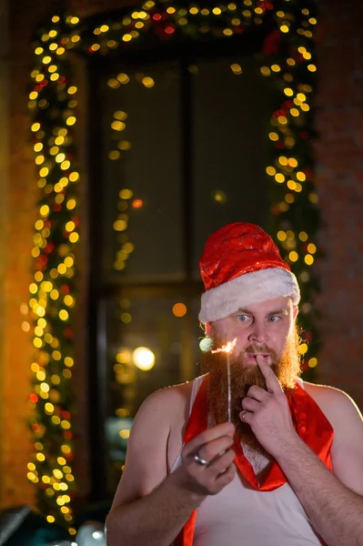 Weihnachtsmann mit Weihnachtsfunkeln im Urlaub. Ein Mann mit rotem Bart und Weihnachtsmannmütze feiert das neue Jahr. Frohes neues Jahr und Weihnachten. — Stockfoto