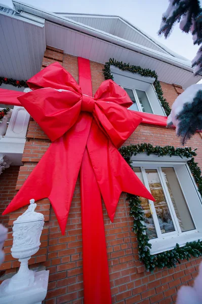 A large bow from a red ribbon on the facade of a brick country house. Christmas decoration with coniferous trees on the window. — Stockfoto