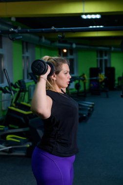 Obez bir kadın kilo vermeye çalışıyor. Şişman sarışınlar, spor salonunda halterli bisepsleri çalıştırıyor. Kötü beslenme alışkanlıkları ve kendini kontrol edememe yüzünden çok fazla ağırlık var..