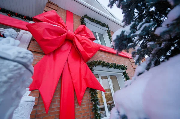 Fasad av en tegelstuga i nyårspynt. Stor röd rosett på väggen i huset. Julgran längs fönstret. — Stockfoto