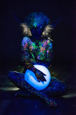 Floresan tozuyla boyanmış bir kadın küresel bir lamba tutuyor. Renkli vücut spreyiyle bir kızın bacaklarının yakınlaştırılması. Yuvarlak neon gece lambası.