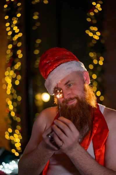Kerstman met kerst schittert op vakantie. Een man met een rode baard in een kerstmuts viert het nieuwe jaar. Geluk met Kerstmis. — Stockfoto