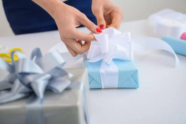 女人在新的一年里用礼物包裹箱子。 女性手的特写。 为母亲节准备一个惊喜。 把纸和带子包起来生孩子. 设计师正在打蝴蝶结. — 图库照片