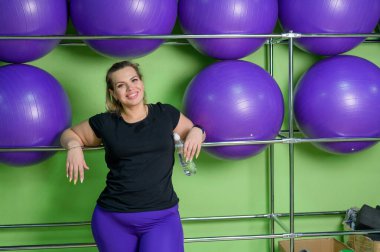 Bir spor kulübünde yoğun eğitimden sonra kadın su içiyor. Şişko sarışın spor salonunda dinleniyor..