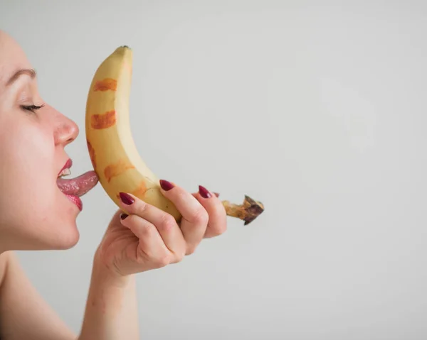 Närbild av ansiktet, läppar, tungan av en ung, europeisk flicka slickar en stor gul, Söt banan. — Stockfoto