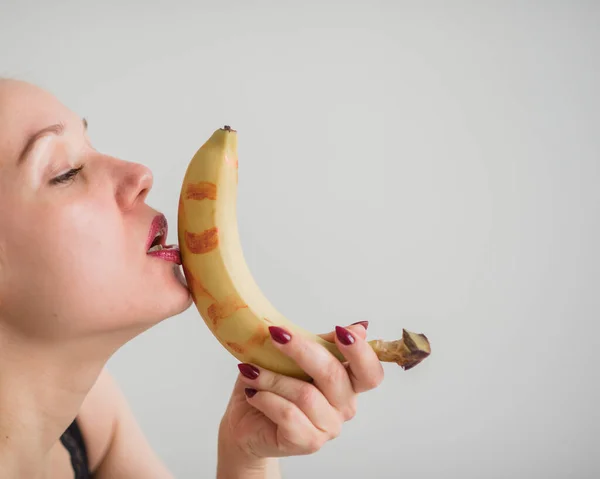 Primo piano del viso, labbra, lingua di una giovane ragazza europea che lecca una grande banana gialla e dolce . — Foto Stock