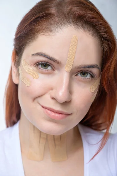 Retrato de una mujer pelirroja con cintas en la cara de color de piel para el rejuvenecimiento. Una forma alternativa de combatir las arrugas . — Foto de Stock