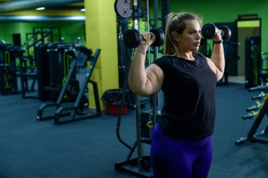 Obez bir kadın kilo vermeye çalışıyor. Şişman sarışınlar, spor salonunda halterli bisepsleri çalıştırıyor. Kötü beslenme alışkanlıkları ve kendini kontrol edememe yüzünden çok fazla ağırlık var..