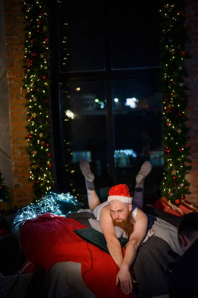 Bad Santa Claus en el fondo de las decoraciones navideñas. Un hombre en un traje de Santa Claus después de la corporación de Año Nuevo . —  Fotos de Stock