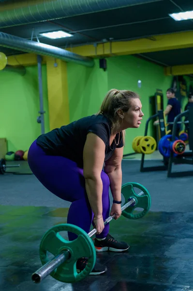 Kövér európai nő foglalkozik fitness egy súlyzóval a tornateremben. Egy kövér lány halálos emelést csinál.. — Stock Fotó