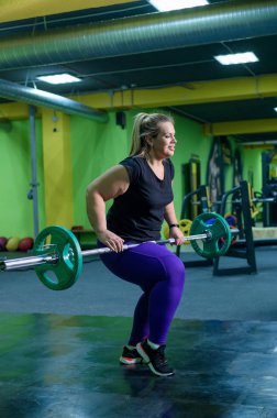 Şişman Avrupalı kadın spor salonunda halterle spor yapıyor. Şişman bir kız kaldırıyor..
