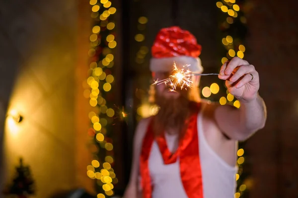 Kerstman met kerst schittert. Een man met een rode baard in een kerstman hoed maakt grapjes een glamoureuze foto. — Stockfoto